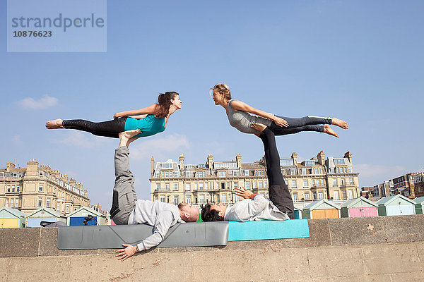 Männer und Frauen praktizieren akrobatisches Yoga an der Wand am Strand von Brighton