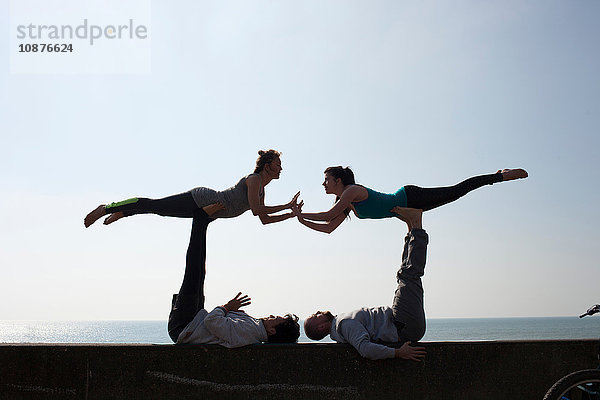 Symmetrische Silhouetten von Männern und Frauen  die akrobatisches Yoga an der Wand am Strand von Brighton praktizieren