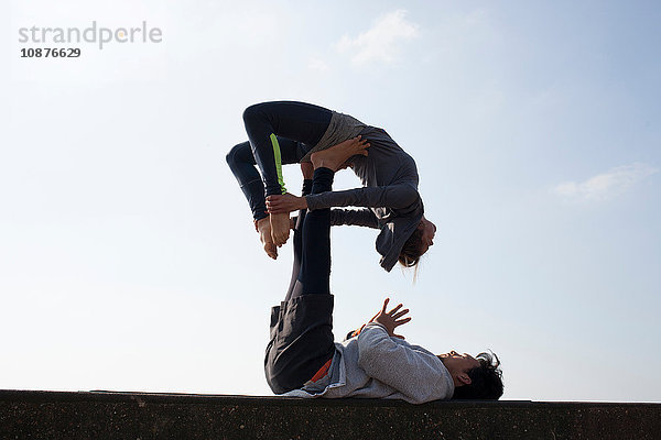 Silhouette eines Mannes und einer Frau  die akrobatisches Yoga praktizieren  an einer Wand vor blauem Himmel