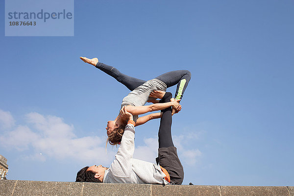 Mann und Frau an der Wand üben akrobatisches Yoga