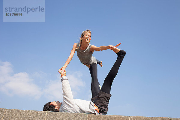 Mann und Frau an der Wand üben akrobatisches Yoga