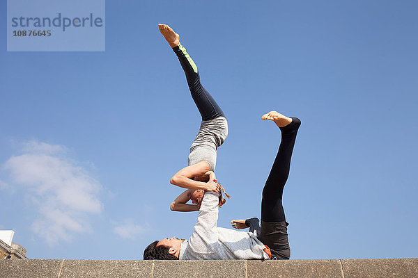 Mann und Frau praktizieren akrobatisches Yoga vor blauem Himmel