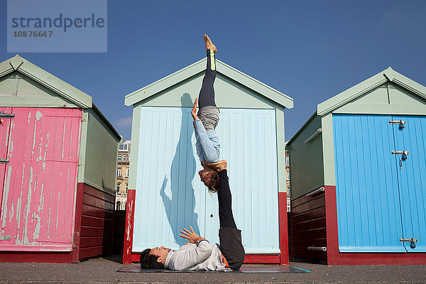 Mann und Frau praktizieren akrobatisches Yoga vor Strandhütten am Strand von Brighton Beach