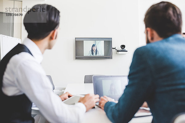 Über-Schulter-Ansicht von Geschäftsleuten bei einer Videokonferenz mit einer Geschäftsfrau