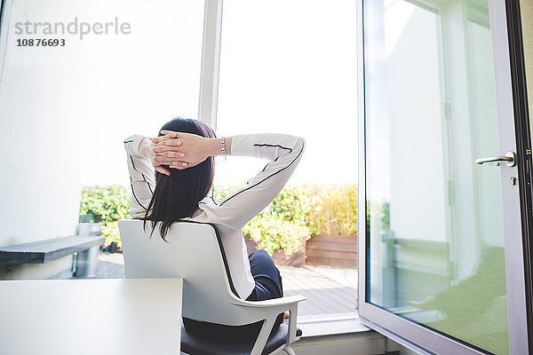 Junge Geschäftsfrau entspannt sich im Büro und schaut aus den Terrassentüren