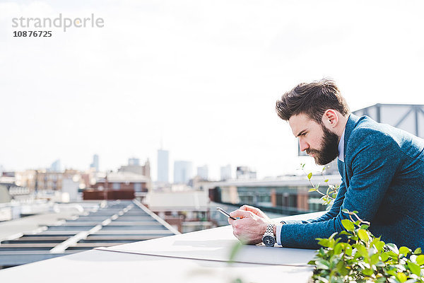 Junger Geschäftsmann liest Smartphone-Text auf Büro-Dachterrasse