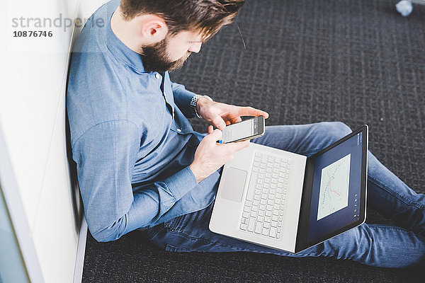 Junger Mann sitzt im Büro und simst mit seinem Smartphone