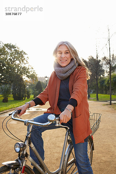 Reife Frau im Park auf dem Fahrrad  die lächelnd in die Kamera schaut
