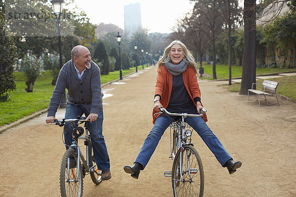 Lächelndes Fahrradpärchen auf baumgesäumtem Weg im Park