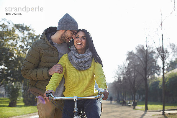 Mittelgroßer erwachsener Mann umarmt lächelnde mittelgroße erwachsene Frau auf Fahrrad im Park