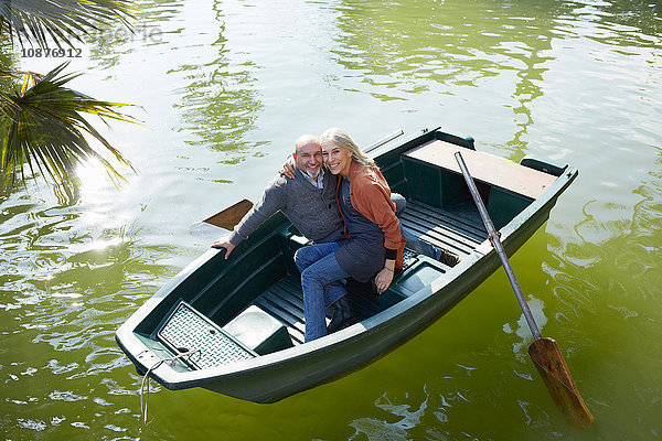 Paar im Ruderboot auf dem See umarmt sich und schaut lächelnd in die Kamera