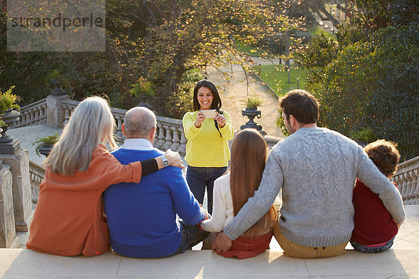 Mittlere erwachsene Frau  die ein Smartphone benutzt  um ein Familienfoto im Park zu machen