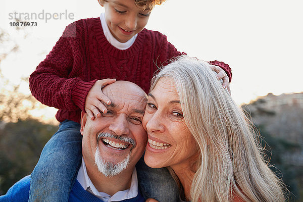 Großeltern mit dem Enkel auf den Schultern  der lächelnd in die Kamera schaut