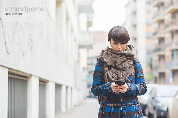 Junge Frau geht auf der Straße und benutzt ein Smartphone