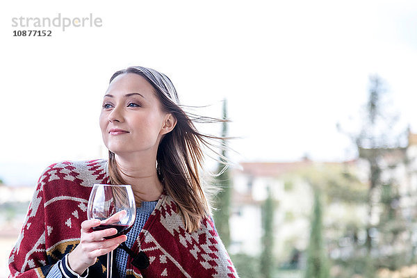 Frau hält ein Glas Rotwein und schaut lächelnd weg