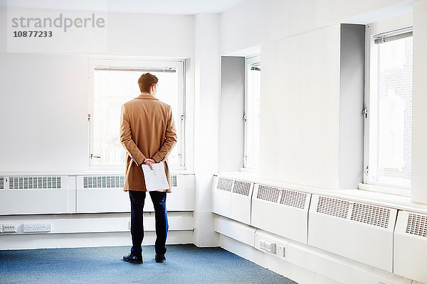 Rückansicht eines Mannes in einem leeren Büro  Hände hinter dem Rücken aus dem Fenster blickend