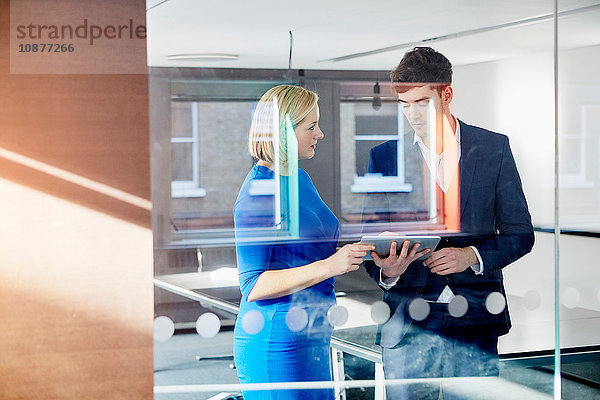 Blick durch Glastrennwand von Kollegen  die ein digitales Tablett halten