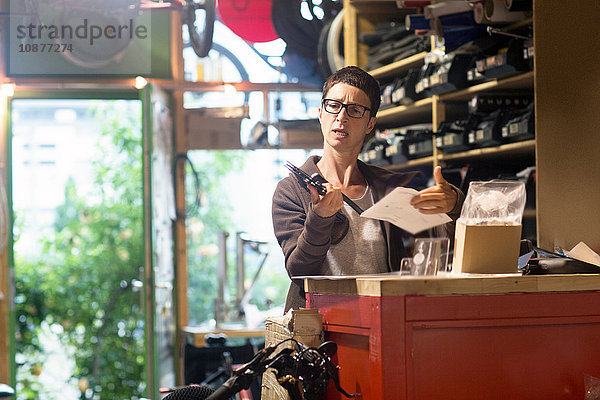 Frau am Schalter in Fahrradwerkstatt mit Fahrradteil und Papierkram