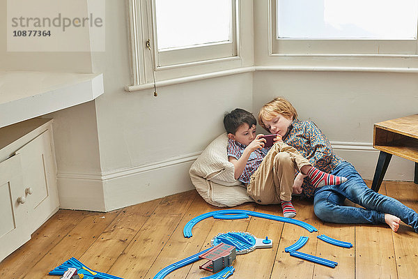 Zwei Jungen  die drinnen sitzen und auf ein Smartphone schauen