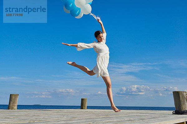 Junge Frau tanzt auf einem Holzsteg  hält einen Haufen Luftballons