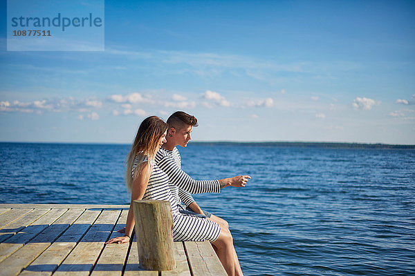 Ehepaar sitzt auf einem Holzsteg und schaut sich die Aussicht an