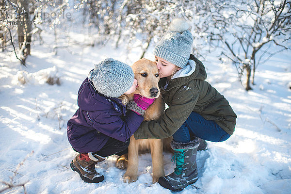 Zwei junge Mädchen  Hund umarmend  in verschneiter Landschaft
