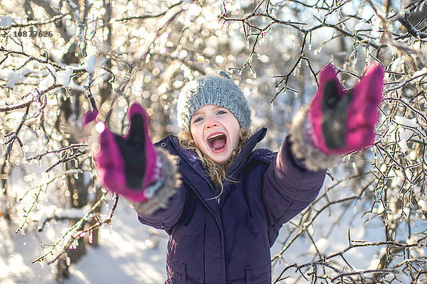 Junges lachendes Mädchen mit ausgestreckten Armen in verschneiter Landschaft