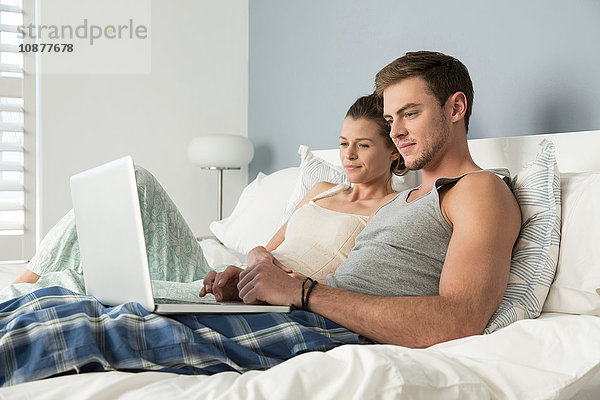 Junges Paar liegt im Bett und liest Buch und Laptop