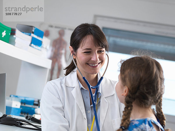 Pädiatrische Ärztin  die in einer Klinik die Brust eines jungen Mädchens mit einem Stethoskop abhört