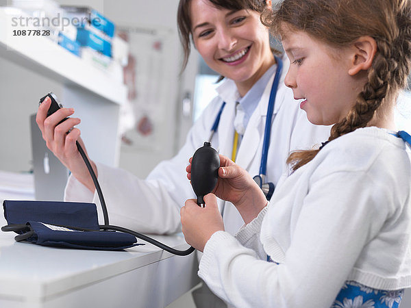Mädchen mit Arzt  der die Blutdruckmanschette betrachtet