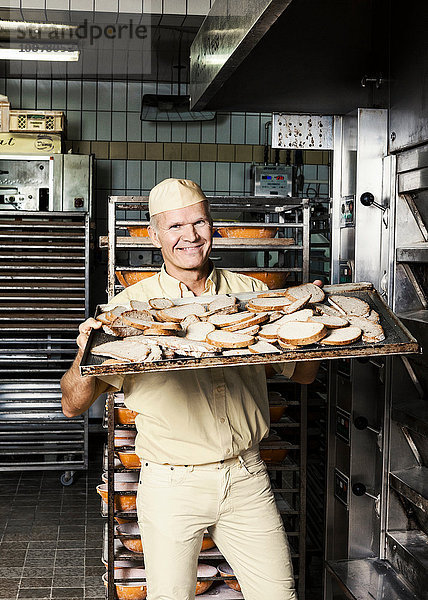 Fröhlicher Bäcker schiebt das Blech mit dem geschnittenen Brot in den Ofen