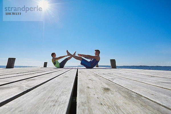 Mitteldistanzansicht des Paares auf dem Pier von Angesicht zu Angesicht bei Sit-ups