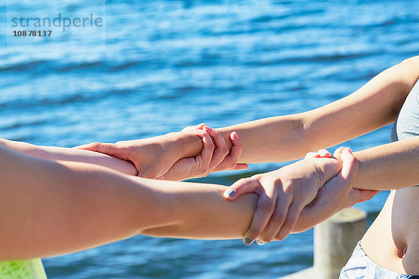 Schrägansicht von Frauen vor dem Ozean  die sich an den Handgelenken festhalten