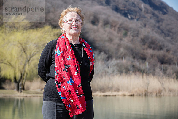 Ältere Frau mit Schal vor dem See schaut lächelnd in die Kamera