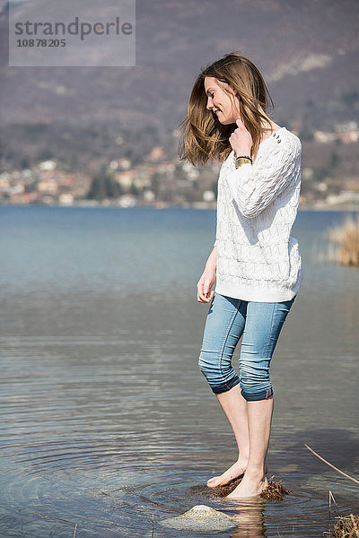 Seitenansicht eines Teenager-Mädchens mit knöcheltief zusammengerollter Jeans im Wasser