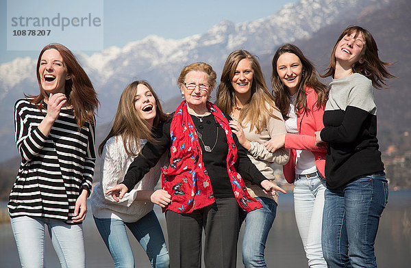 Großmutter mit Enkelinnen vor schneebedeckten Bergen mit lächelndem Blick in die Kamera
