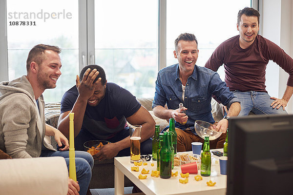 Gruppe von Männern sieht Sportereignis im Fernsehen mit Snacks und Bier lächelnd