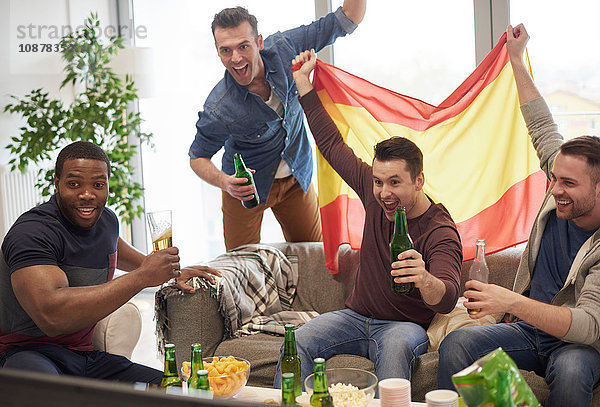 Gruppe von Männern  die im Fernsehen ein Sportereignis mit spanischer Flagge verfolgen und feiern