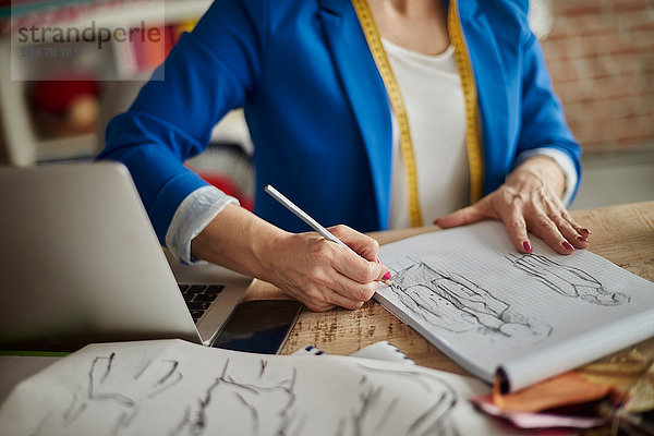 Ausschnitt einer Frau  die am Schreibtisch sitzt und Modedesign skizziert