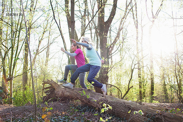 Seitenansicht von Frauen im Wald  die über umgefallenen Baum springen