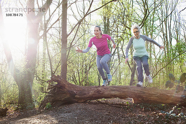 Frauen im Wald springen über umgefallenen Baum