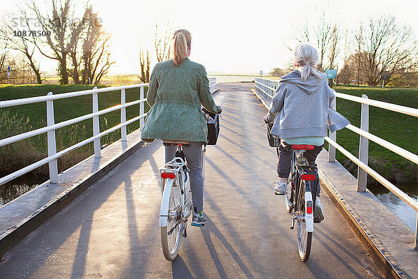 Rückansicht von Rad fahrenden Frauen auf der Brücke über den Fluss