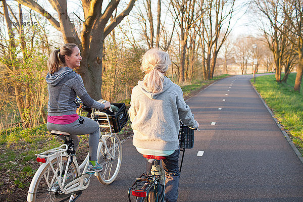Rückansicht von Frauen  die auf einer von Bäumen gesäumten Straße Rad fahren