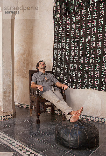 Mann sitzt mit erhobenen Füßen auf Puff  Marrakesch  Marokko