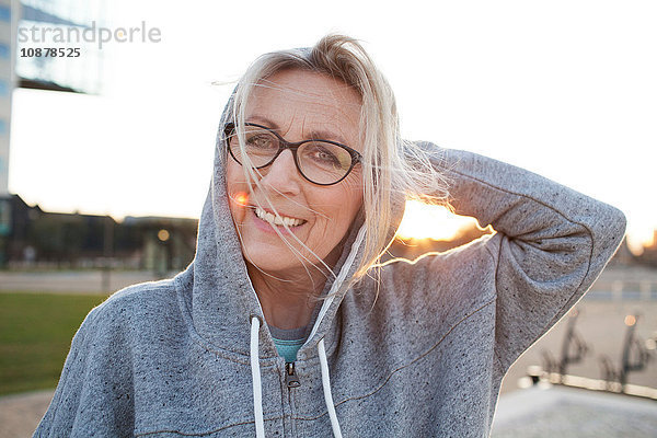 Porträt einer Frau mit Brille und Kapuzenoberteil  die lächelnd in die Kamera schaut