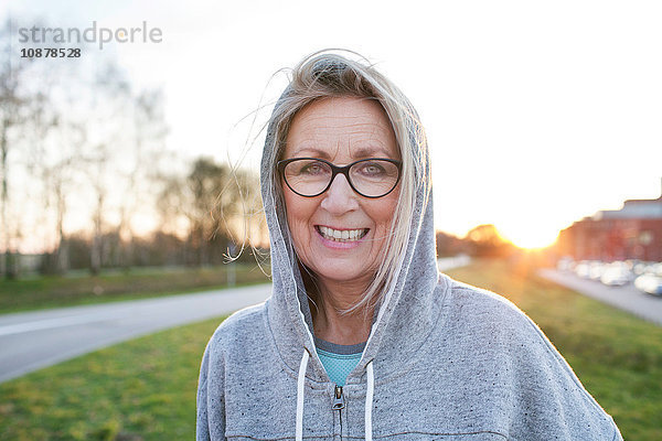 Porträt einer Frau mit Brille und Kapuzenoberteil  die lächelnd in die Kamera schaut