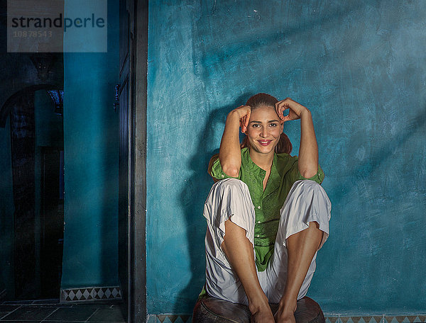 Frau sitzt auf einem Puff und schaut lächelnd in die Kamera  Marrakesch  Marokko
