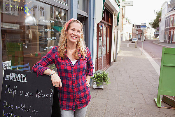 Frau vor einem Laden  die sich gegen einen Rahmen lehnt und lächelnd in die Kamera schaut