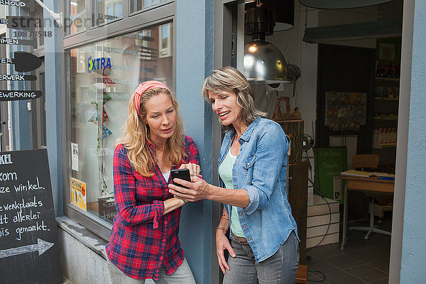 Frauen stehen in einer Ladentür und schauen auf ein Smartphone