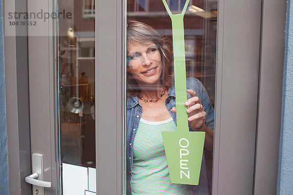 Blick durch die gläserne Ladentür einer Frau  die ein Schild offen hält